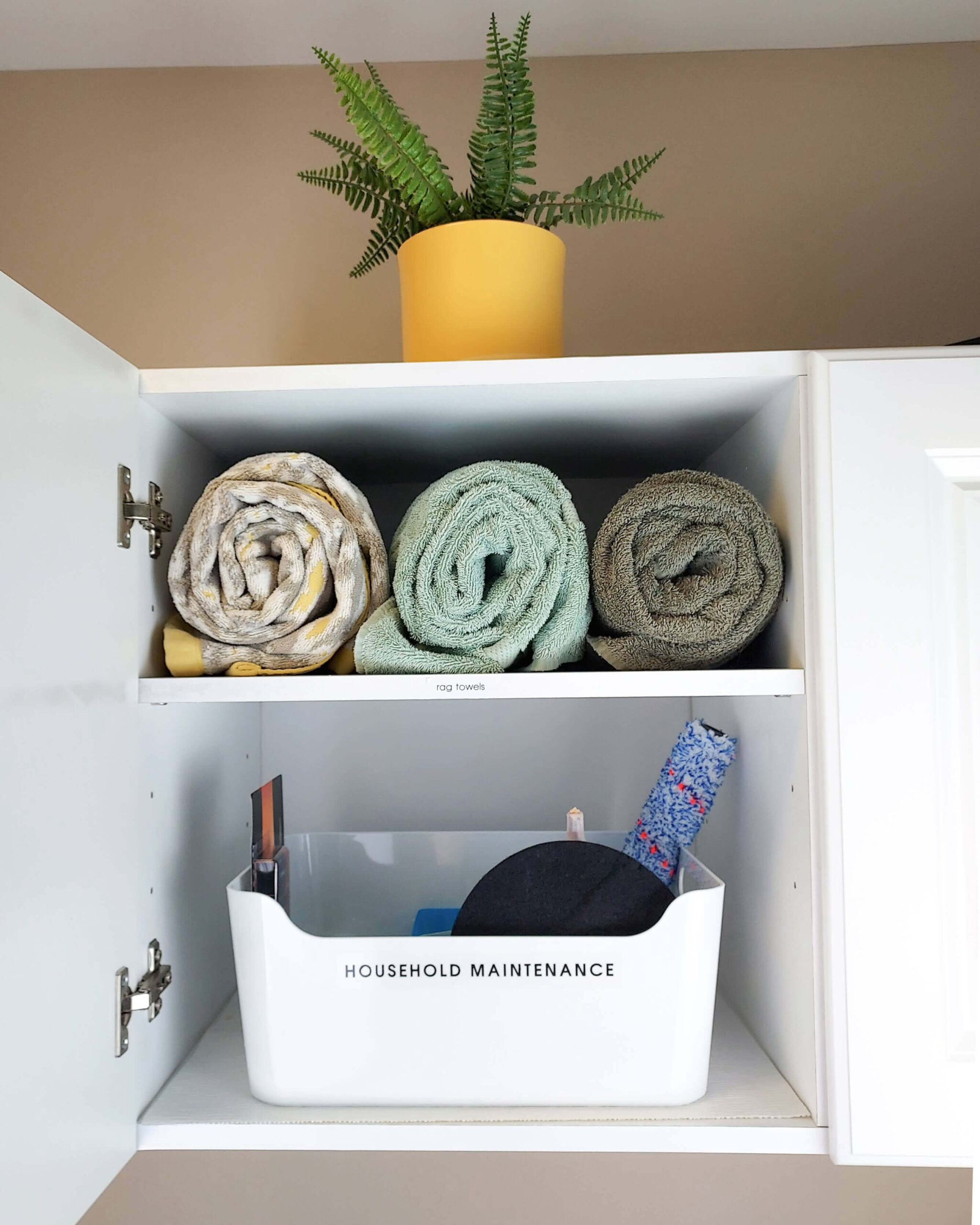 an organized laundry room cabinet with neatly rolled towels and a house maintenance bin