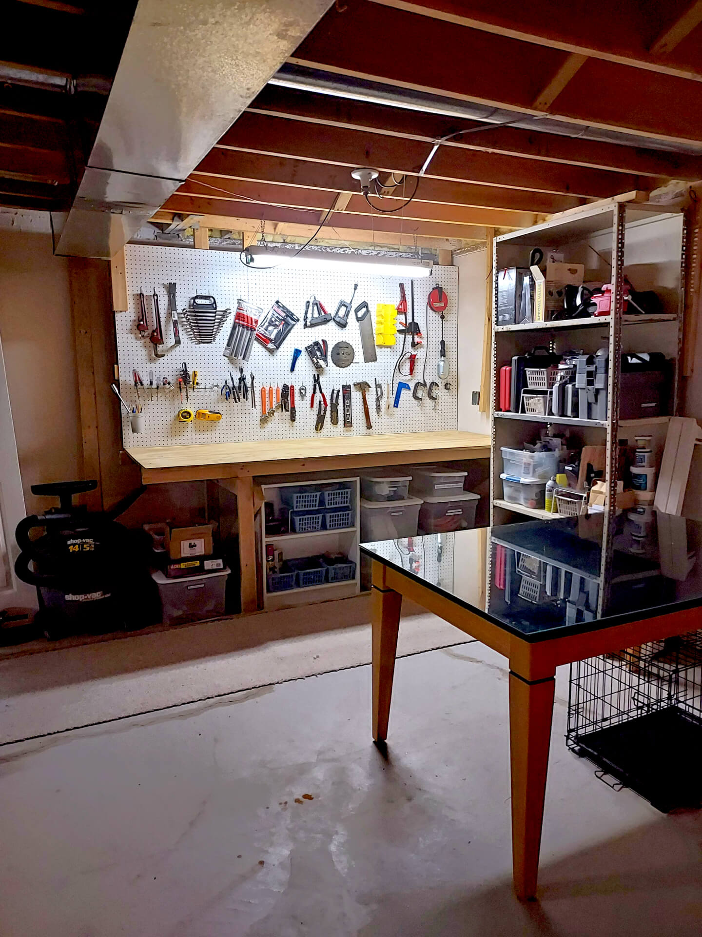 Organized basement workshop with a cleared workbench, tools arranged on a pegboard, sorted storage bins, and open floor space.