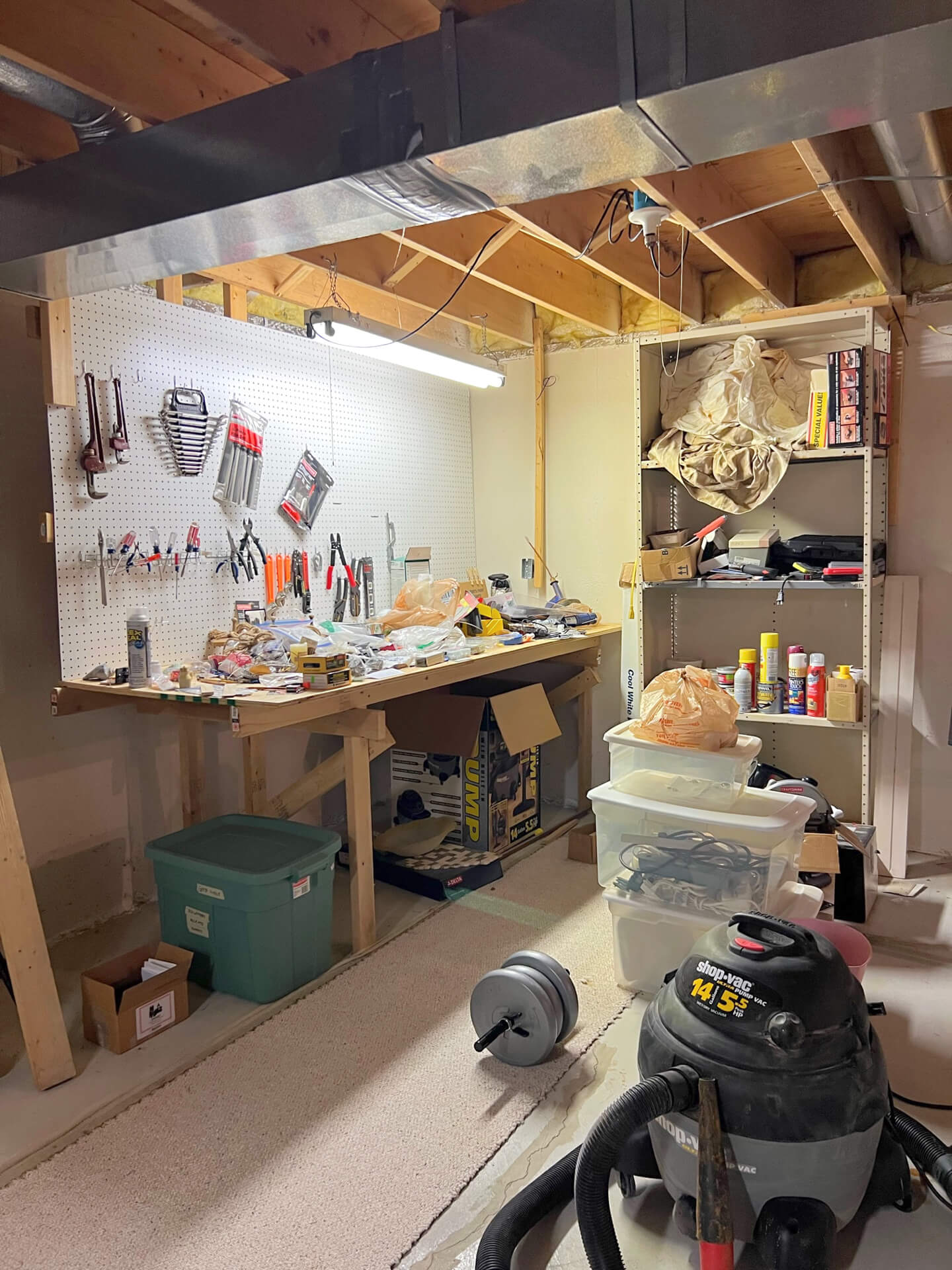 Basement workshop before professional organizing, with a cluttered workbench, crowded shelving, and storage bins on the floor.