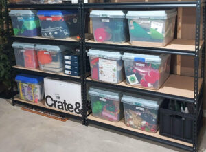 Organized Halloween and Christmas decorations in labeled clear storage bins on basement shelving.