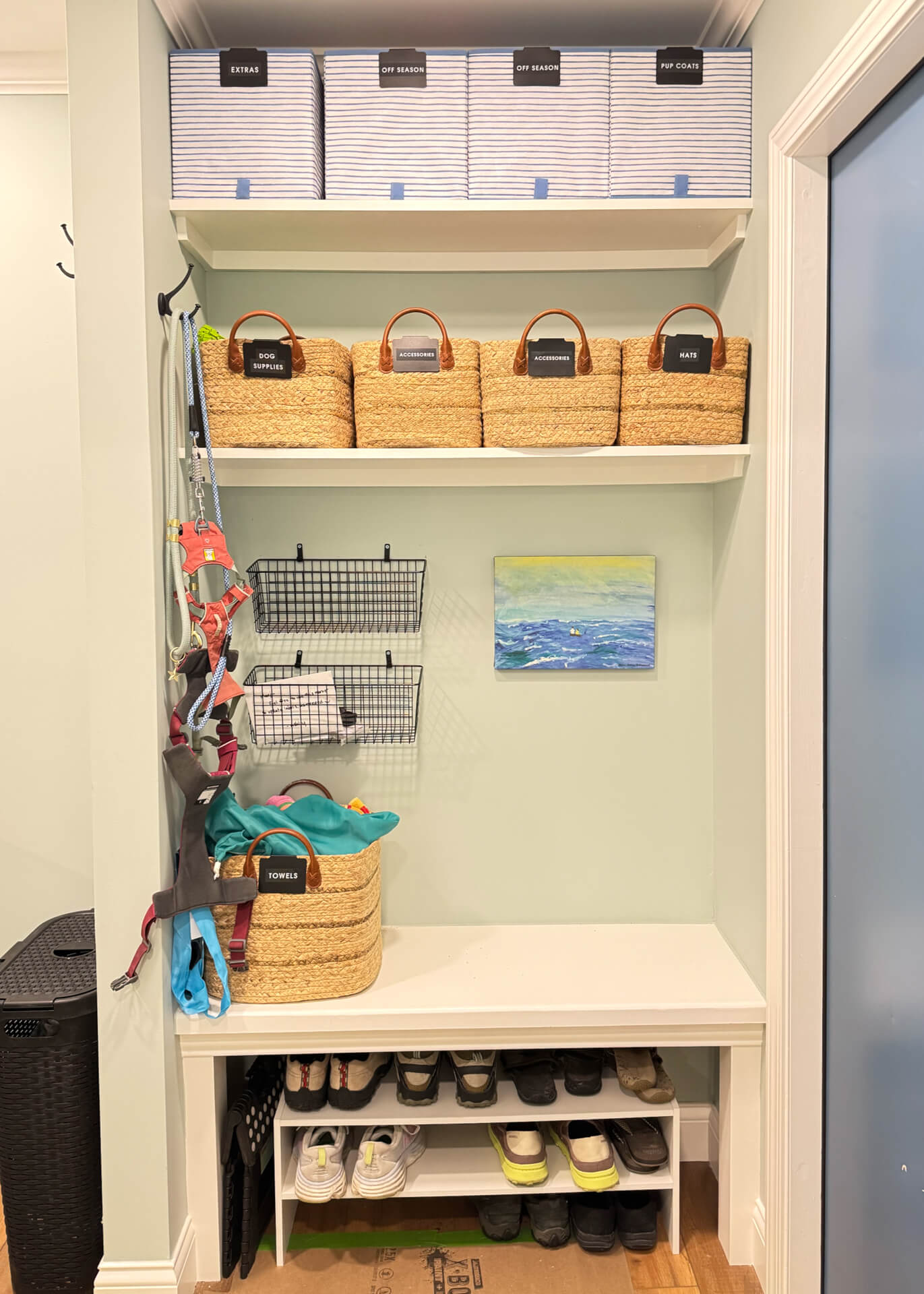 Professionally organized mudroom with labeled storage baskets, wall hooks, shoe shelves, and built-in bench.